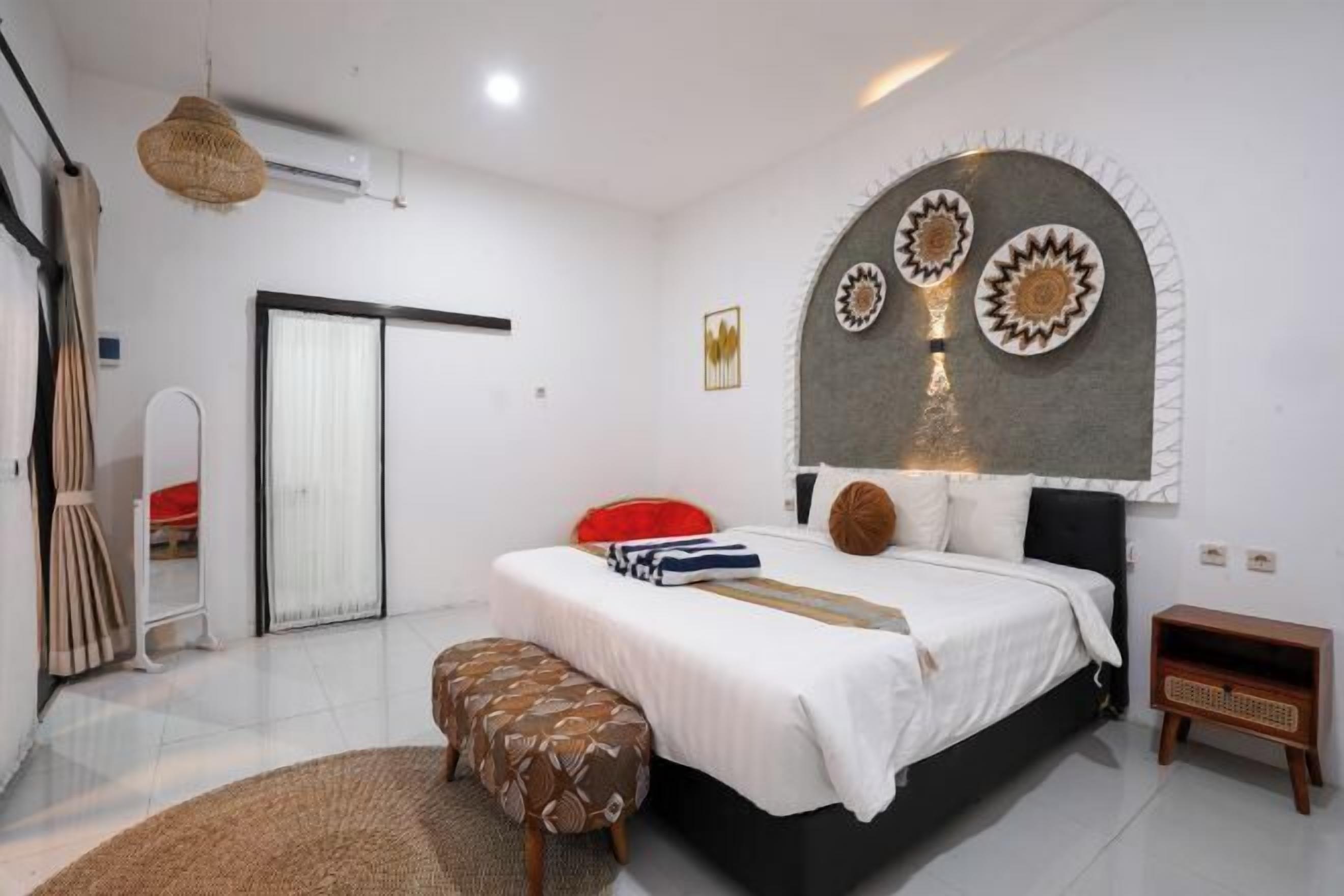 A bedroom with a bed, a bench, a small wooden side table, a mirror, and a decorative wall.
