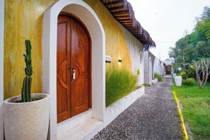 Un bâtiment avec une porte en bois, un cactus en pot et un chemin de gravier.