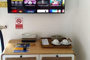Una habitación con televisión mostrando carteles de películas, un cartel de prohibido fumar y una mesa de madera con un menú y un juego de té.