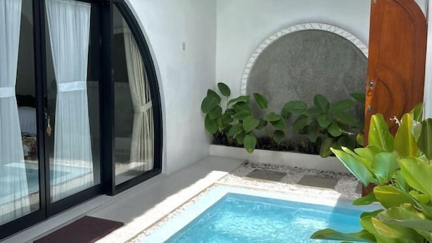 Un área de piscina privada con puerta de vidrio, pared de piedra con plantas y puerta de madera.