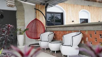 A patio area with wicker furniture, a hanging red chair, and a potted plant.