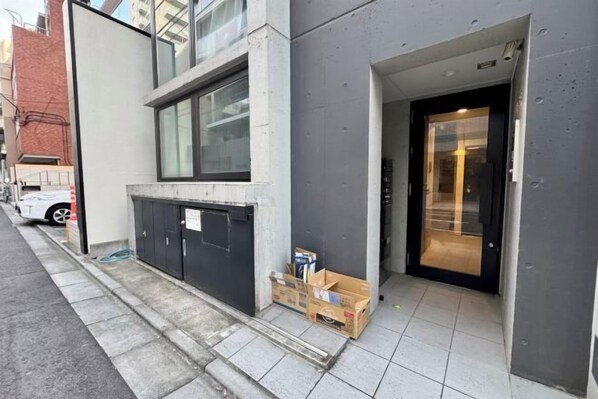 A building entrance with a glass door, a small step leading up to it, and a few cardboard boxes on the ground. - FAREakihabara　ONE (Tokyo)