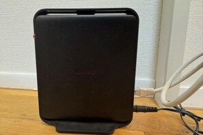 A black portable power bank with a cable connected to it, placed on a wooden surface. - FAREakihabara　ONE (Tokyo)
