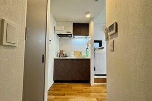 A narrow hallway leading to a compact kitchen with a wooden floor, a built-in oven, and a microwave. - FAREakihabara　ONE (Tokyo)