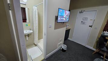 A bathroom with a shower, toilet, sink, and a television mounted on the wall.