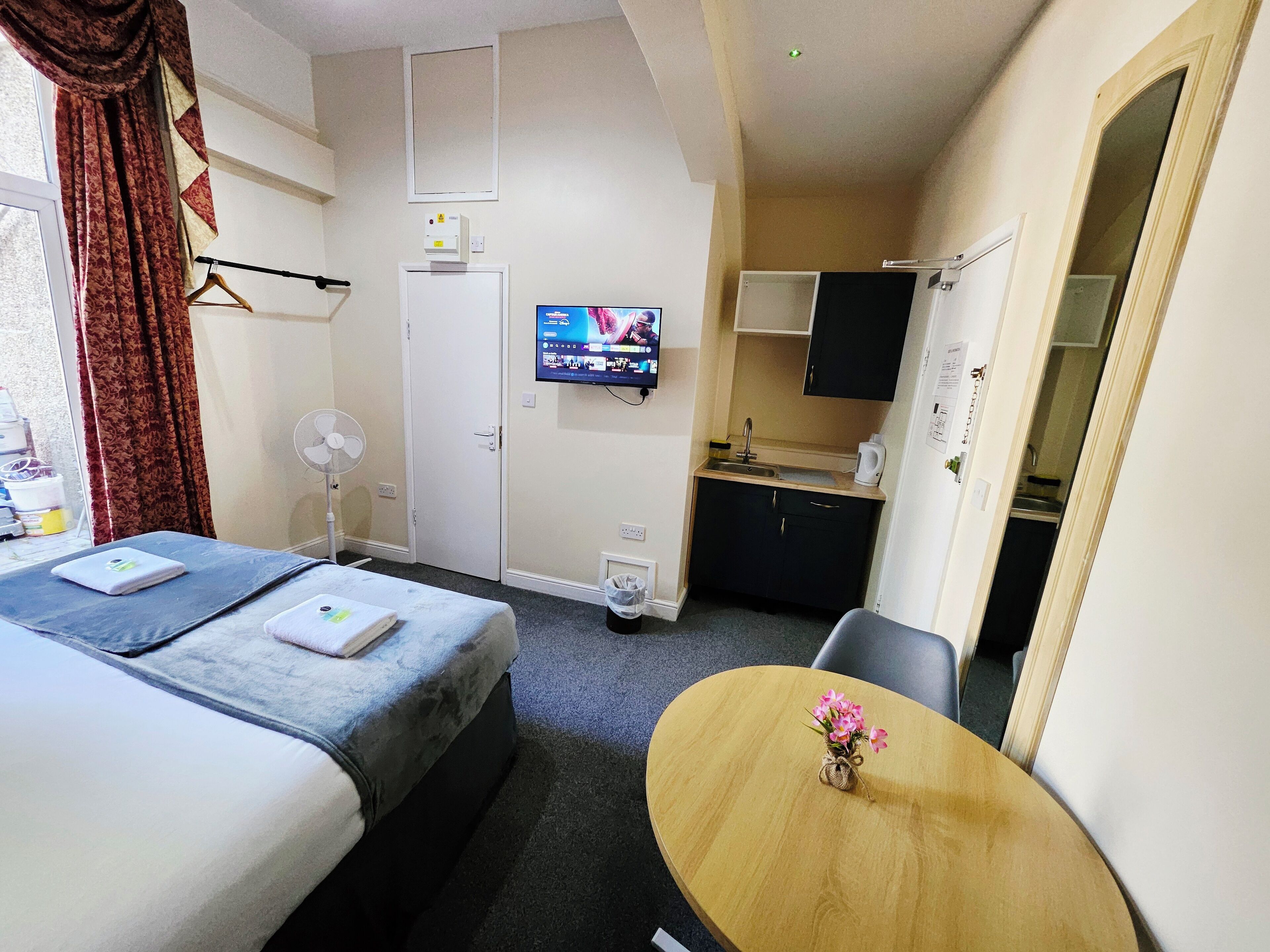 Habitación de hotel con dos camas, televisión, una kitchenette pequeña y una mesa de comedor con flores.