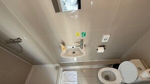 Ein Badezimmer mit Toilette, Waschbecken und Dusche. Ein Handtuchhalter und ein Toilettenpapierhalter sind vorhanden.