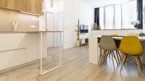 Une cuisine moderne avec des meubles en bois, un coin repas avec deux chaises et un téléviseur fixé au mur.