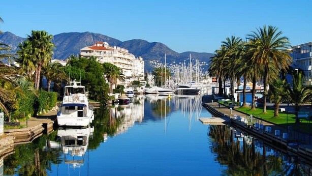 Un port de plaisance avec des bateaux, un bâtiment doté d’un toit rouge et des palmiers.