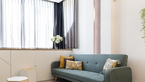 Un salon moderne avec un canapé gris, des tables d’appoint en bois et une fenêtre avec des rideaux.