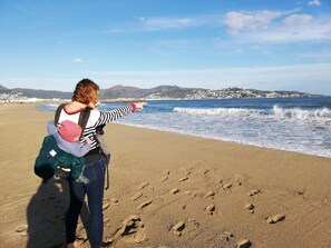 Une personne se trouve sur une plage avec un enfant et désigne la mer du doigt.