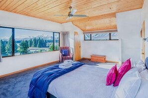 A bedroom with a bed, a chair, a window with a mountain view, and a ceiling fan. - The Lake House (Lake Tekapo)