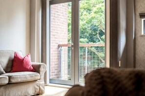 Ein Wohnzimmer mit einer Schiebetür zu einem Balkon, einem Sofa mit einem roten Kissen und einem Blick auf einen Hund.