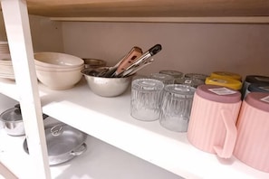 A kitchen shelf with bowls, a colander, and glass jars.