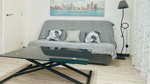A modern living room with a grey sofa, two patterned cushions, a glass coffee table, and a cityscape painting on the wall. - Getaway in Roses: Comfort, Terrace & Shared Pool (Roses)