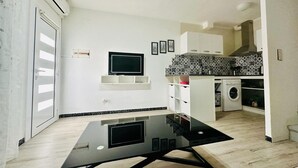 A modern kitchen with a built-in washing machine, a flat-screen TV, and a black glass table. - Getaway in Roses: Comfort, Terrace & Shared Pool (Roses)