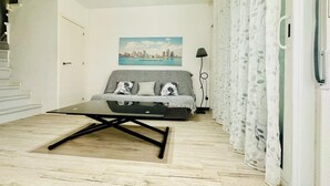 A modern living room with a sofa, a coffee table, and a cityscape painting on the wall. - Getaway in Roses: Comfort, Terrace & Shared Pool (Roses)