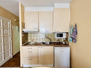 A compact kitchen with a microwave, sink, and a small refrigerator. There are cabinets and a tiled backsplash.
