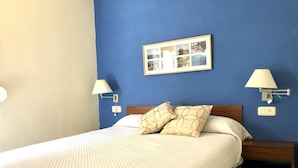 A neatly made bed with a quilted cover, two bedside lamps, a nightstand, and a framed collage on the wall.