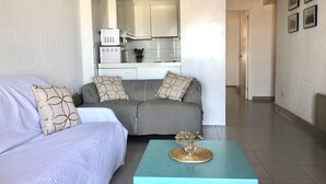 A modern living room with a sofa, a coffee table, and a kitchen area visible through an open doorway.