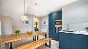 A modern kitchen with a wooden table, pendant lights, and a built-in island with a sink. - Host & Stay The Coachouse at Pilgrim St (Liverpool)