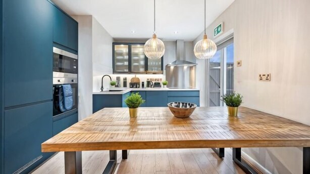 A modern kitchen with a wooden dining table, pendant lights, and a view of the living area. - Host & Stay The Coachouse at Pilgrim St (Liverpool)