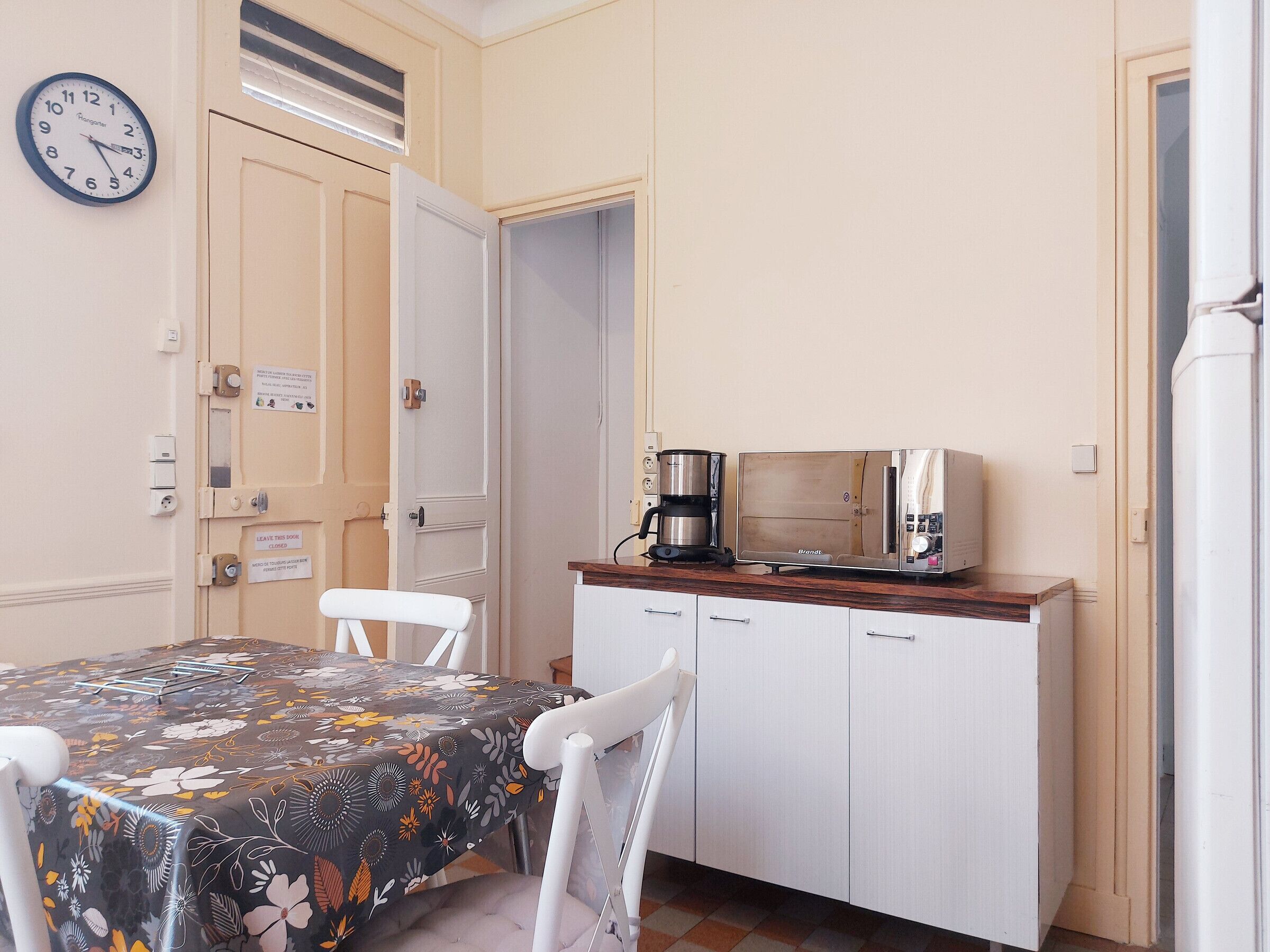 A small kitchen with a table, chairs, a clock, a coffee maker, and cabinets.