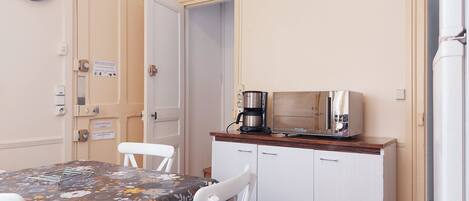 A small kitchen with a table, chairs, a clock, a coffee maker, and cabinets.