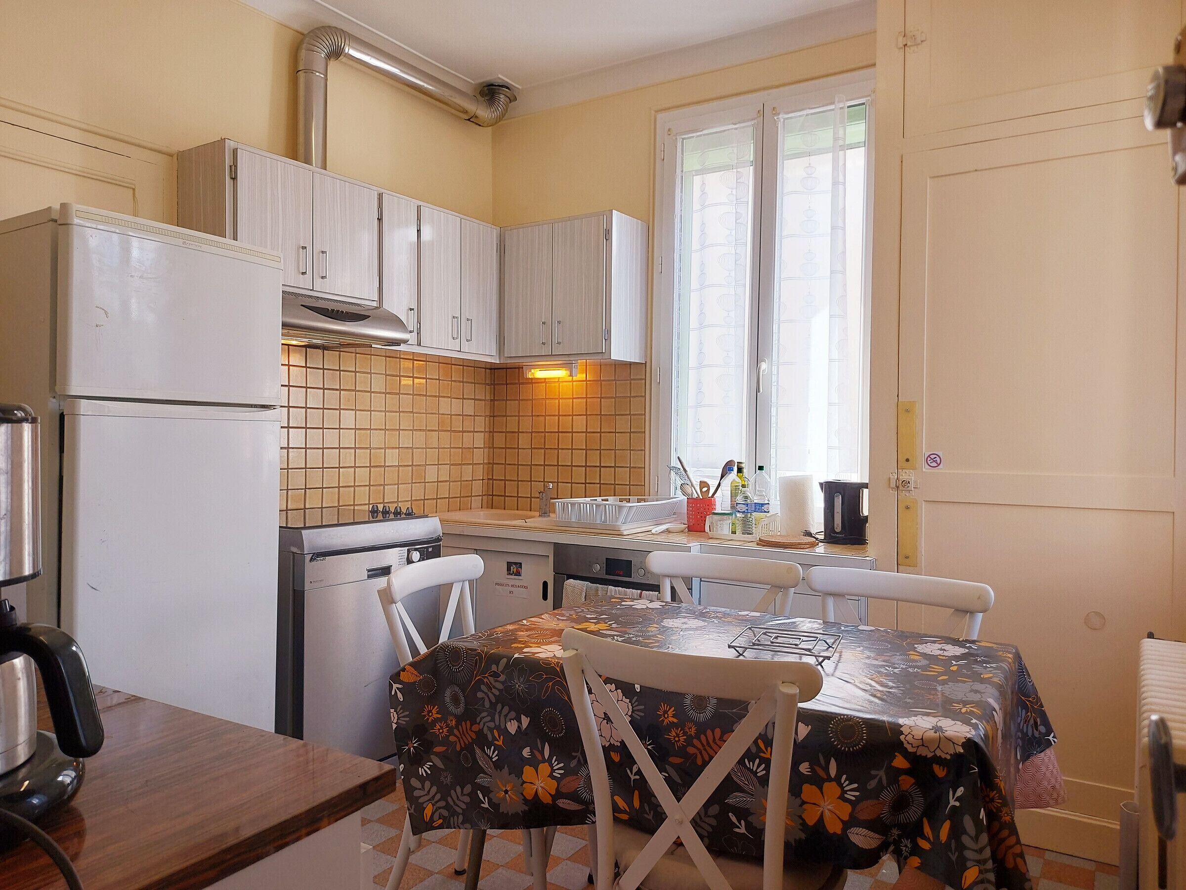 Une cuisine de taille réduite avec des meubles blancs, une cuisinière à gaz, un réfrigérateur et une table à manger avec des chaises.