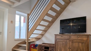 A room with a wooden staircase, a television on a wooden cabinet, and a window with a curtain. - Spacious house with covered terrace and parking in natural area (Méobecq)