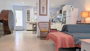 A modern kitchen with white cabinets, a dining area with a table and chairs, and a living room with a sofa and a lamp. - Spacious house with covered terrace and parking in natural area (Méobecq)