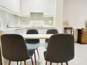 A modern kitchen with white cabinets, a dining table with two chairs, and a wooden cabinet to the side.