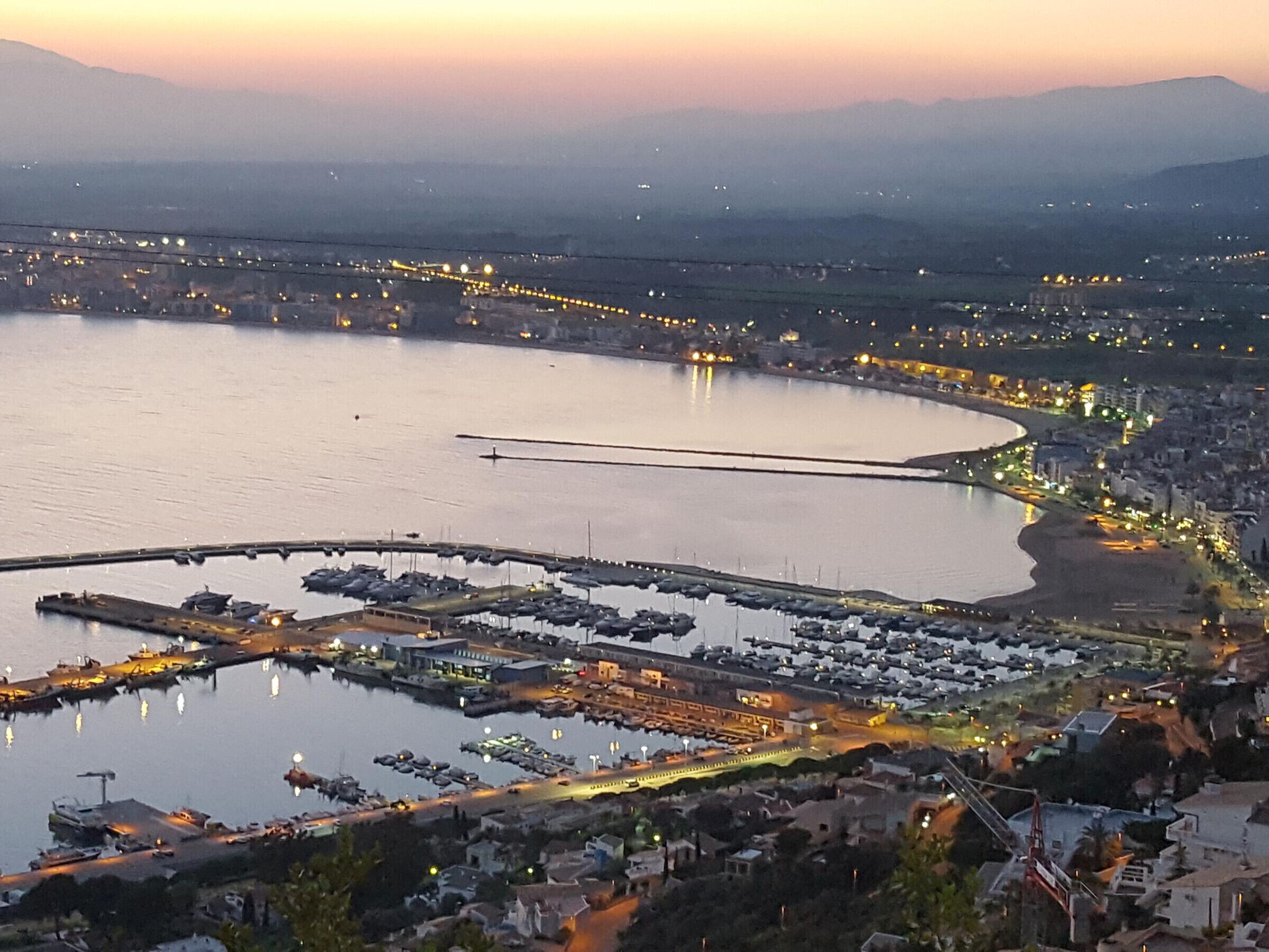 An aerial view of a coastal city with a marina, buildings, and a bridge.
