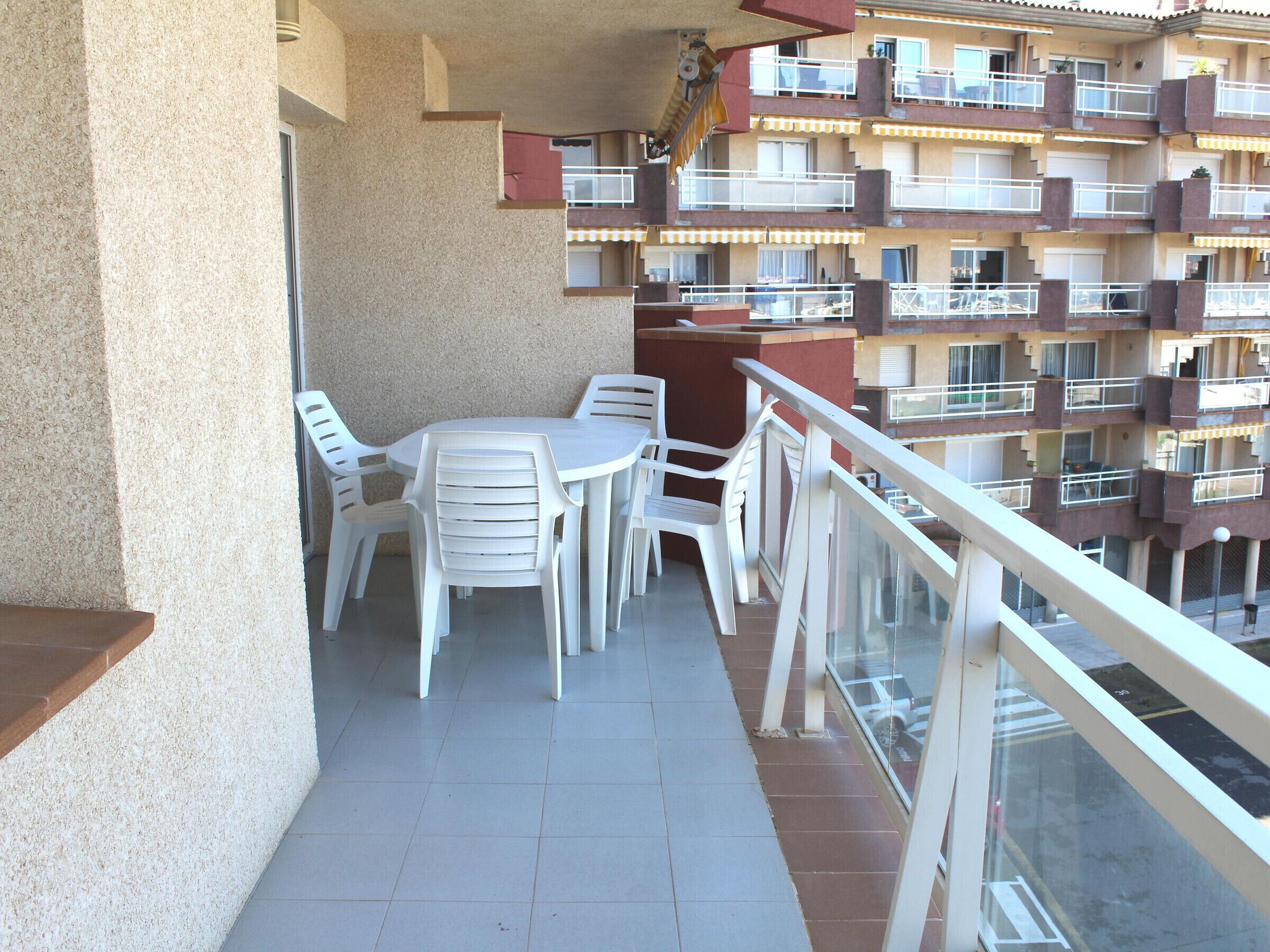 A balcony with a table and chairs, a railing, and a view of a multi-story building with balconies.