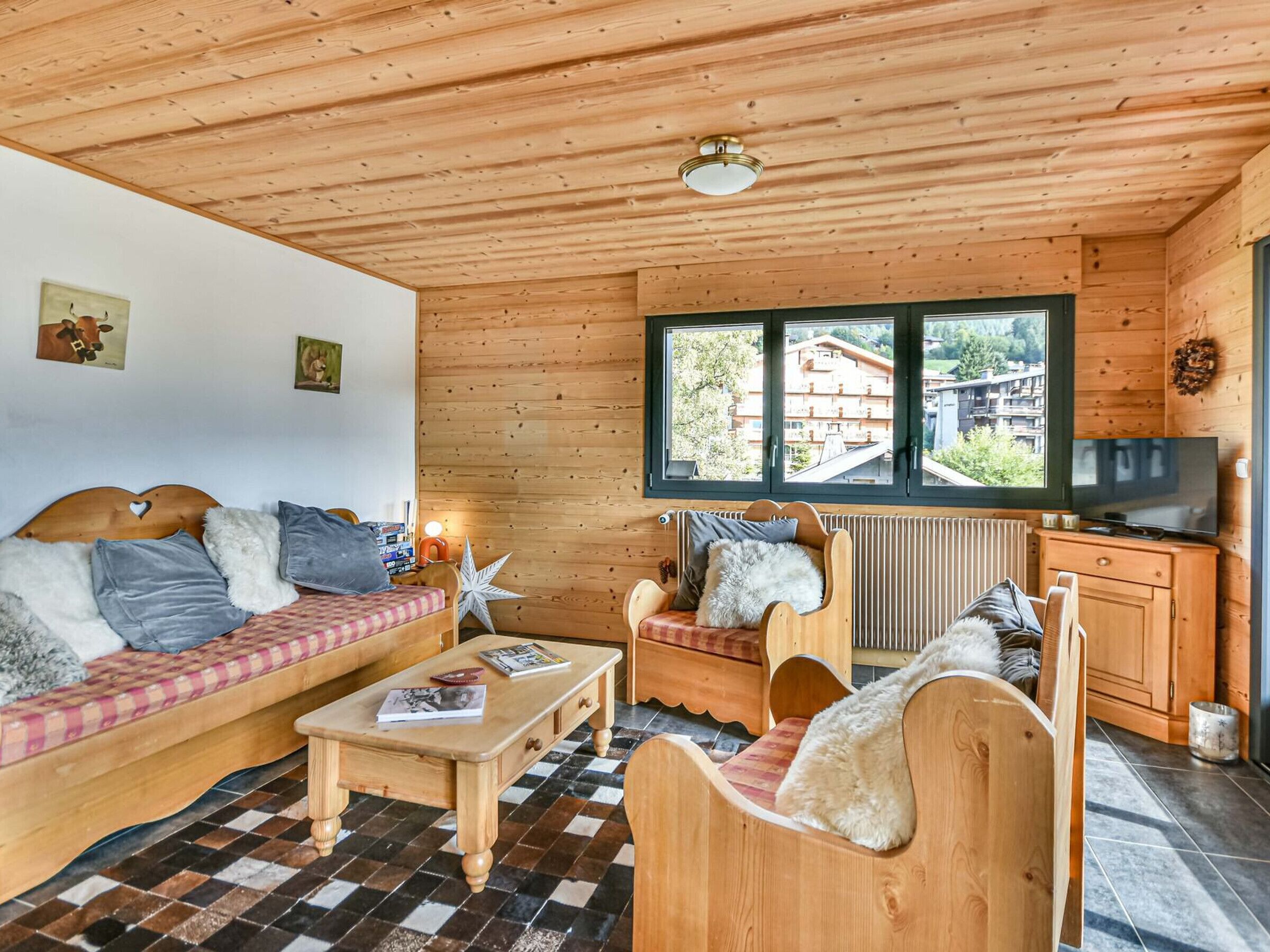 L’intérieur d’un chalet accueillant, avec des murs et un plafond en bois, un canapé, un fauteuil, une table basse et un téléviseur.