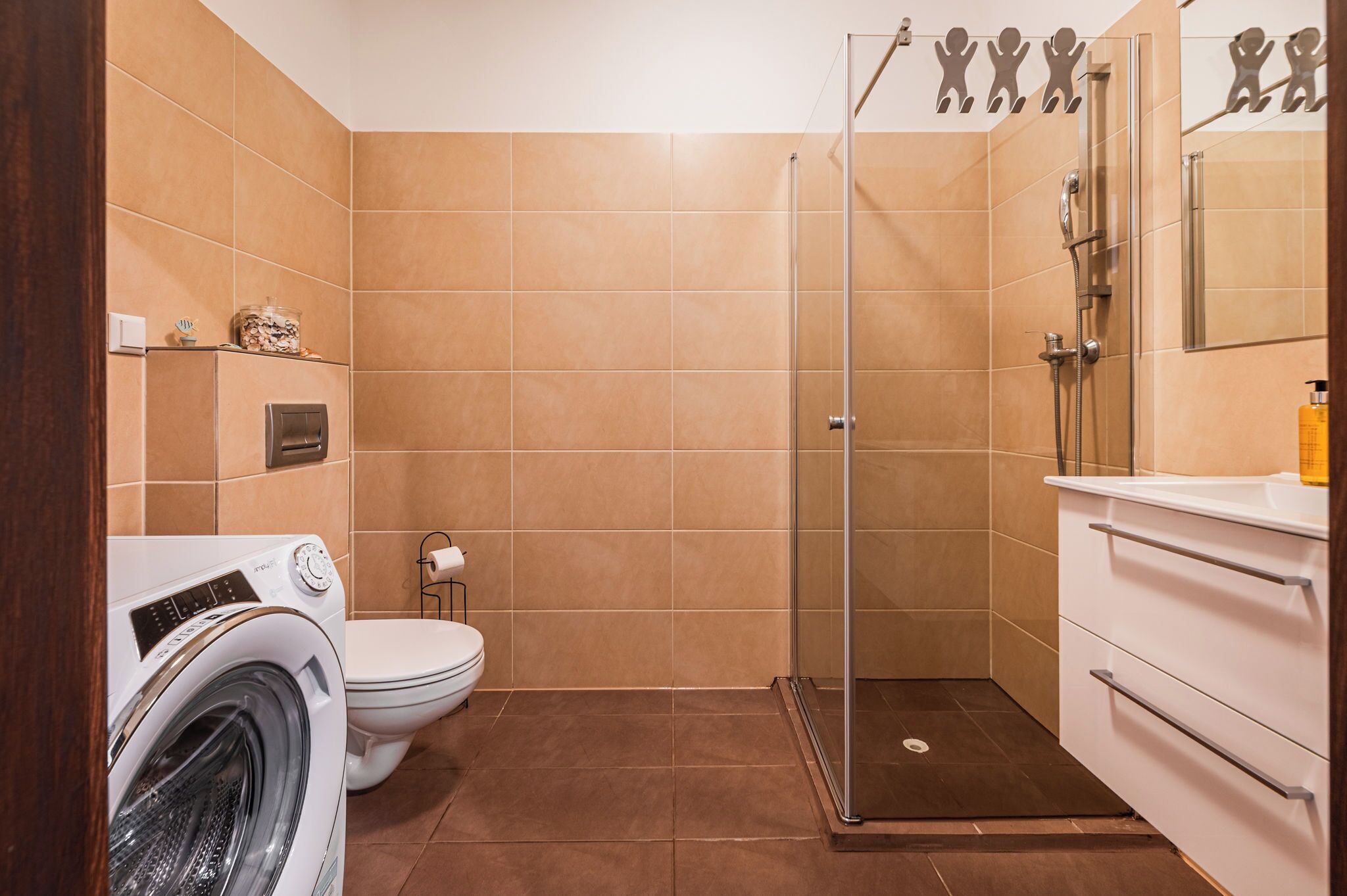 Une salle de bain équipée d’un lave-linge, de toilettes et d’une douche séparée par une paroi en verre.
