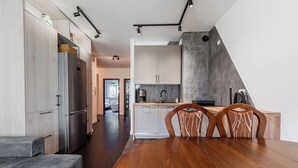 Cozinha moderna com área de jantar, destacando uma grande mesa de madeira e cadeiras, geladeira embutida e uma parede de concreto.