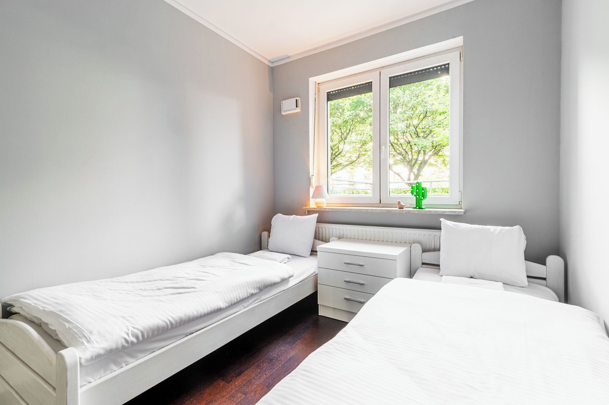 Een slaapkamer met twee bedden, een raam met uitzicht op bomen, een radiator en een nachtkastje.