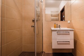 A bathroom with beige tiled walls, a glass shower enclosure, a white sink with a mirror above it, and a towel rack visible in the reflection. - RentPlanet - Apartament Piękna z tarasem (Wrocław)