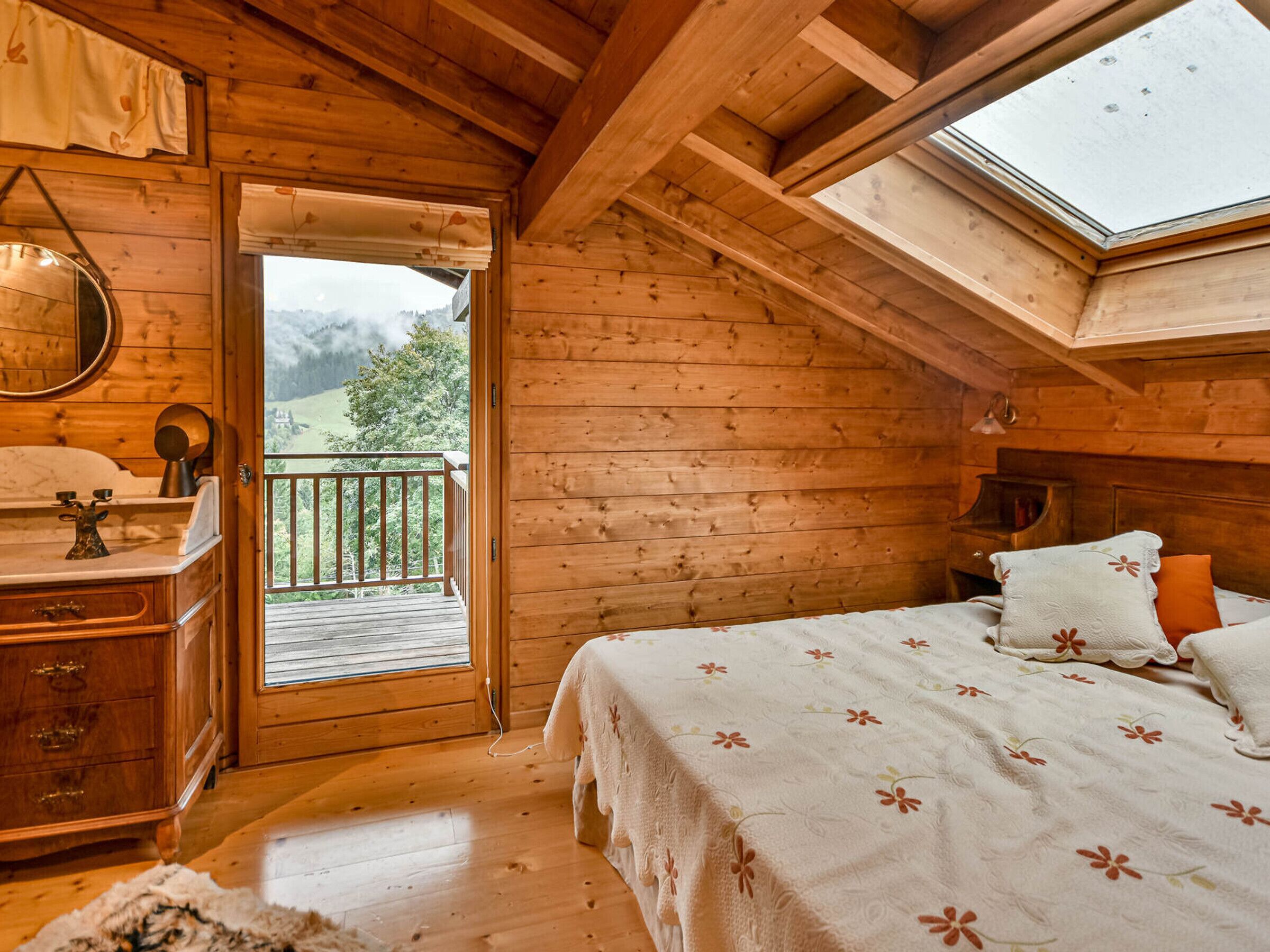 Een houten slaapkamer met een bed, een dressoir en een balkon met uitzicht op de natuur.