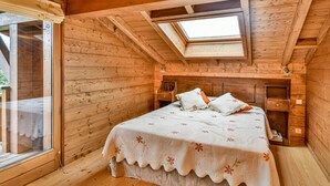 Une chambre à coucher chaleureuse, avec des murs en bois, une lucarne, un lit recouvert d’une literie à motifs floraux et une table de chevet.