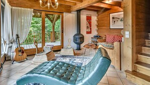Un intérieur de chalet chaleureux avec un plafond en bois, une grande fenêtre, une cheminée et un coin salon confortable.