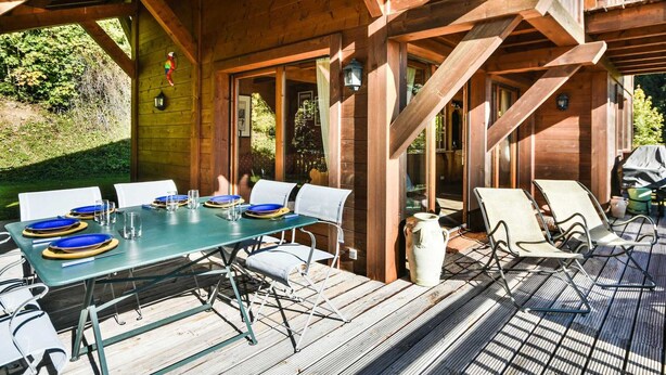 Une terrasse en bois avec une table dressée pour quatre personnes, entourée de chaises.