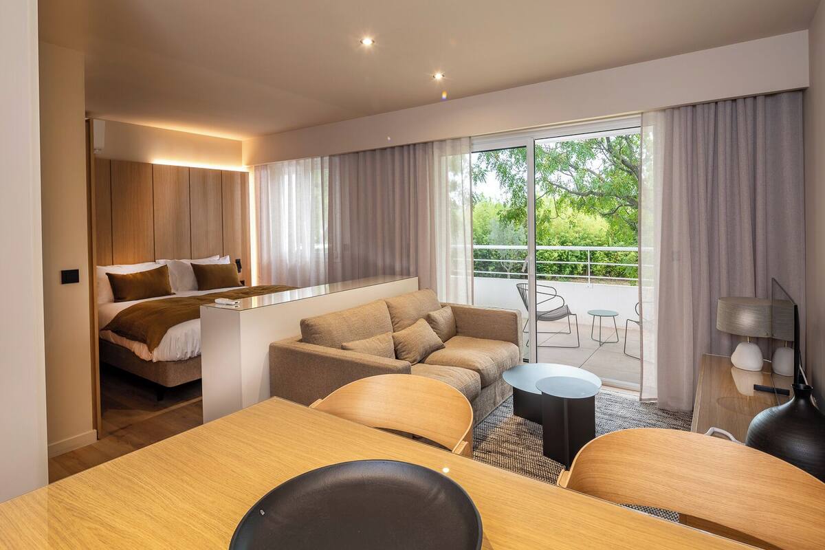 Une chambre d’hôtel moderne dotée d’un grand lit, d’un canapé, d’une table à manger et d’un balcon avec des meubles d’extérieur.