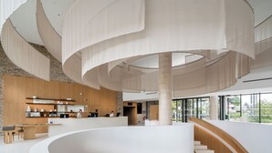 Een modern interieur met een centrale spiraaltrap, een receptiegedeelte met een houten paneelwand en grote ramen met uitzicht op buiten.