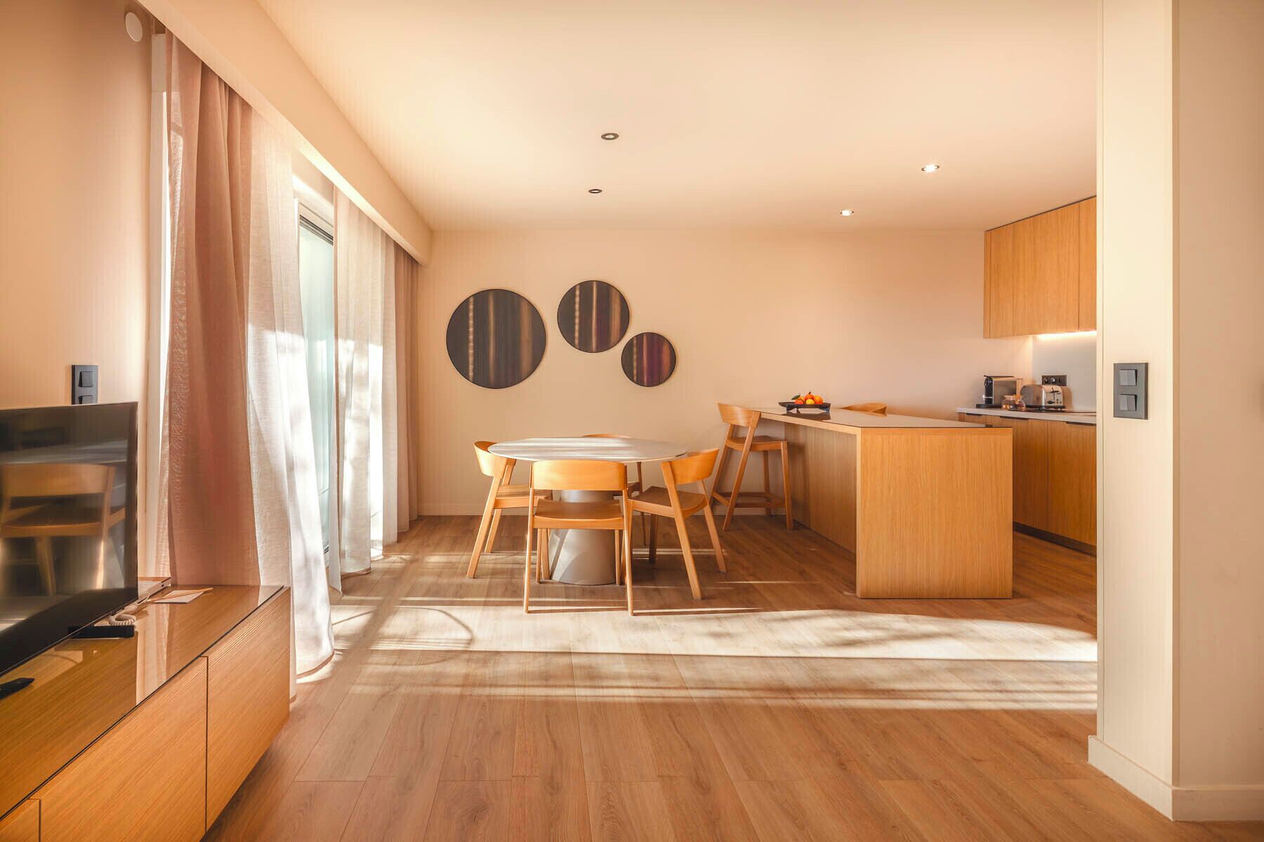 Eine moderne Küche mit Holzschränken, ein Essbereich mit einem runden Tisch und ein Fernseher im Wohnbereich.