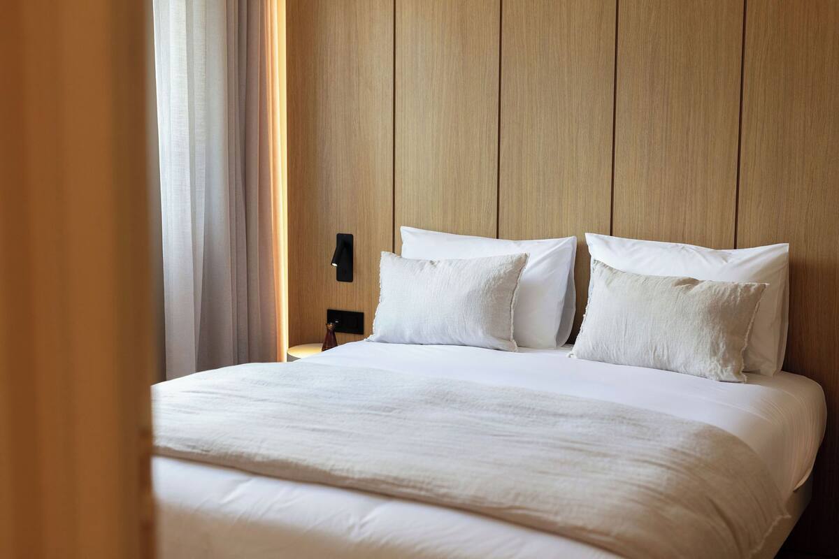 Un lit bien fait, avec du linge de lit blanc, une tête de lit en bois et une table de chevet avec une lampe.