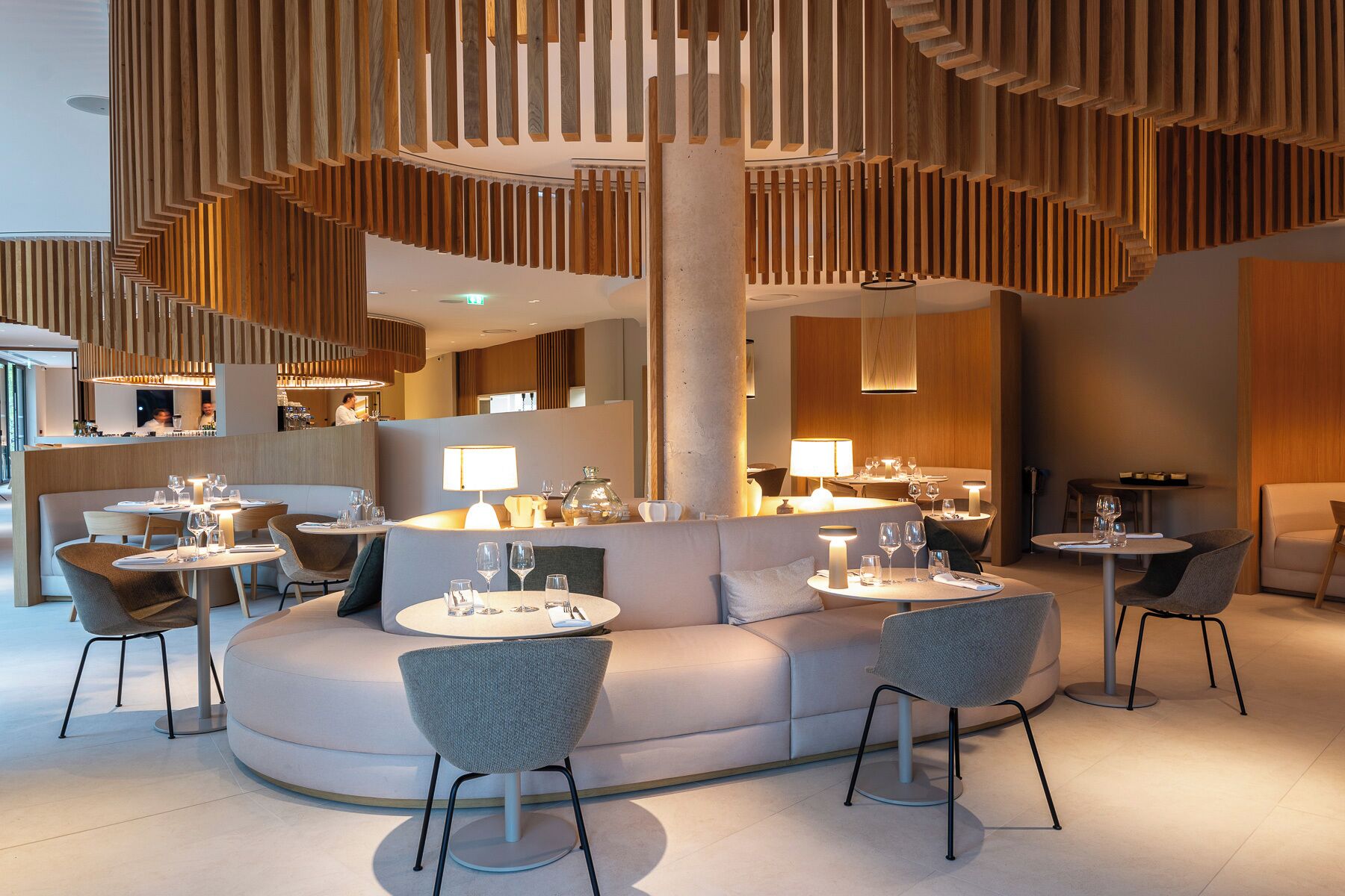 A modern restaurant with round tables, cushioned seating, and wooden paneling.