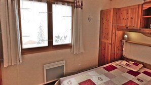 A bedroom with a bed, a window with curtains, a radiator, and wooden furniture. - Comfortable 2-room apartment for 5 with private parking (Le Grand-Bornand)
