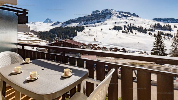 A balcony with a table and chairs overlooking a snowy mountain landscape. - Comfortable 2-room apartment for 5 with private parking (Le Grand-Bornand)